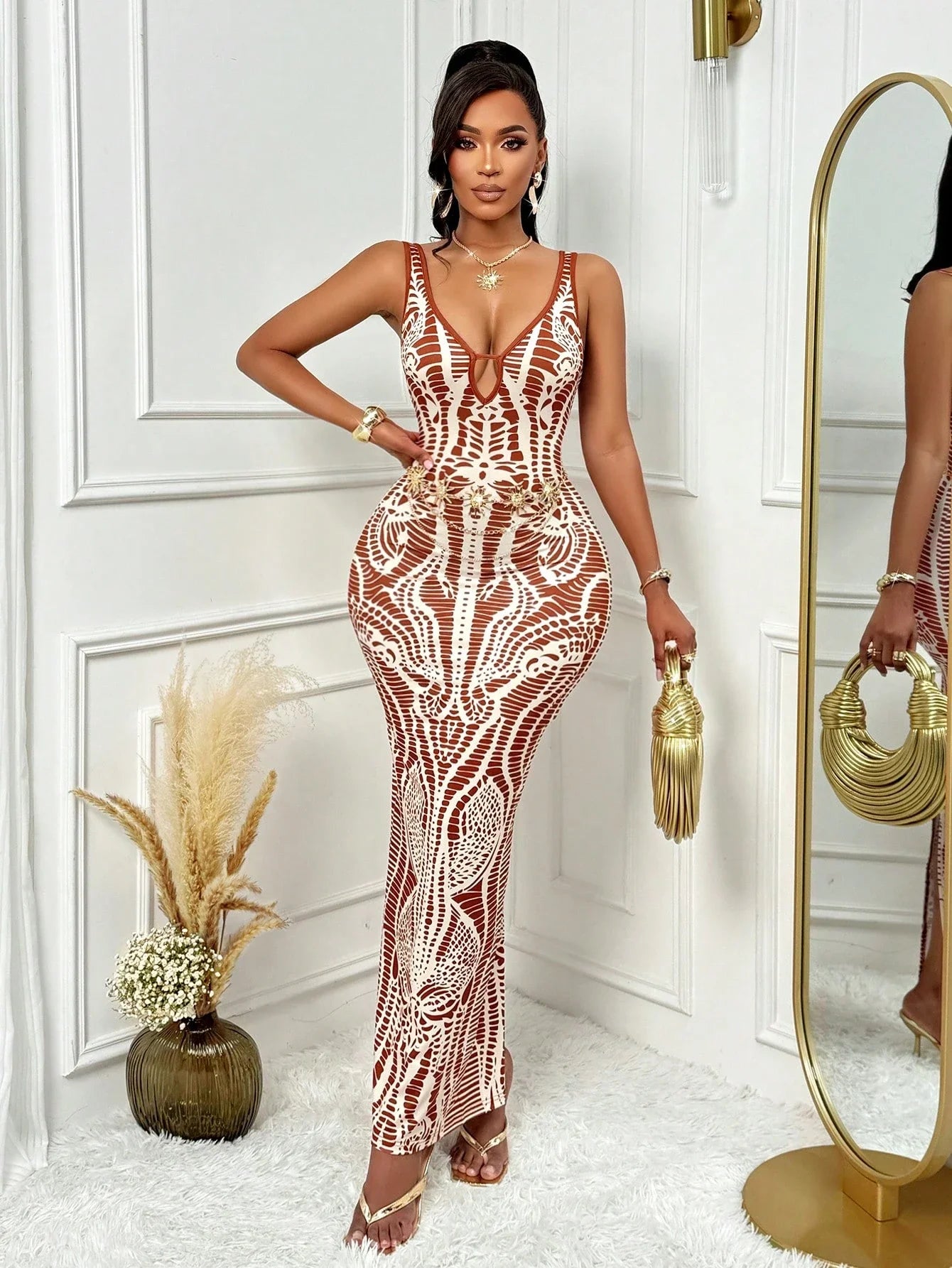 Woman in a patterned dress holding a gold handbag in a stylish interior setting.