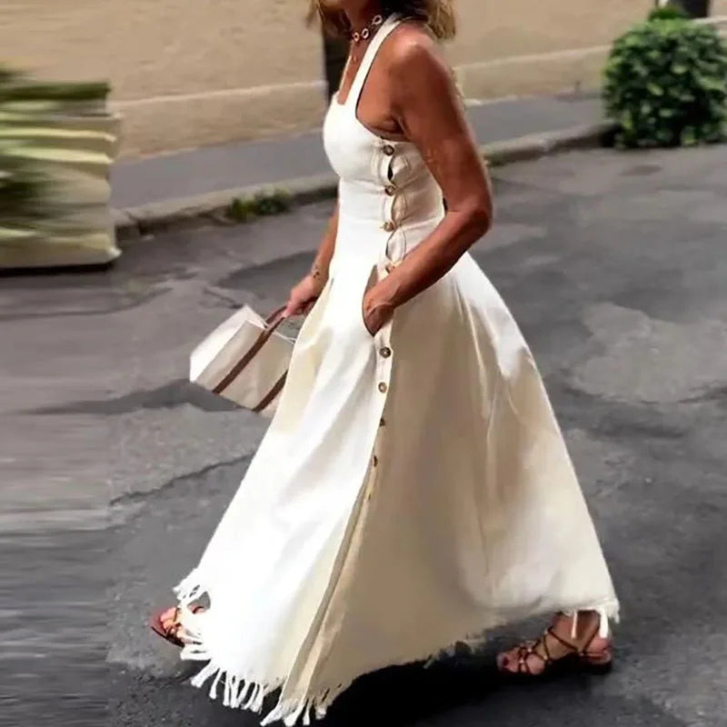 Woman wearing a white dress with buttons and fringes, standing on a street.