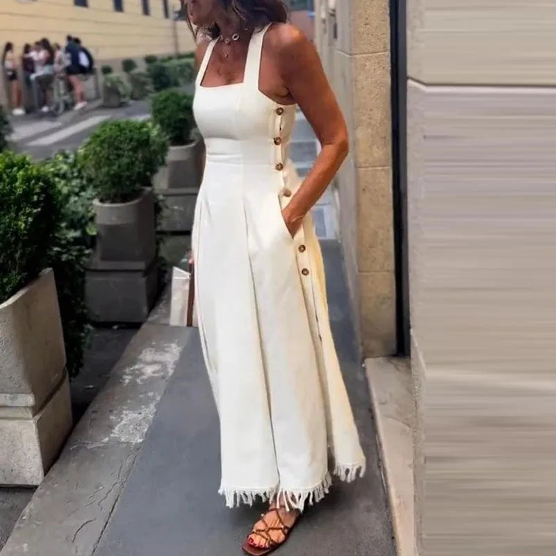 Woman wearing a white dress with buttons and fringe details on a city street.