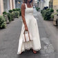 Woman in a white dress holding a handbag on a city street.