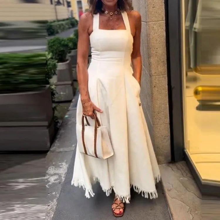 Woman in a white dress with fringe holding a handbag on a city street.