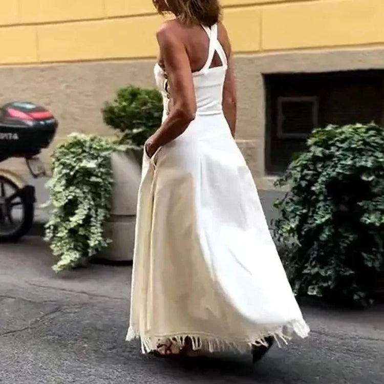 Woman in a white dress walking on a street with a yellow building and green bushes in the background.